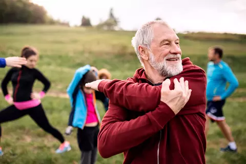Seniorengruppe macht Sport im Freien, ein Mann dehnt sich im Vordergrund.